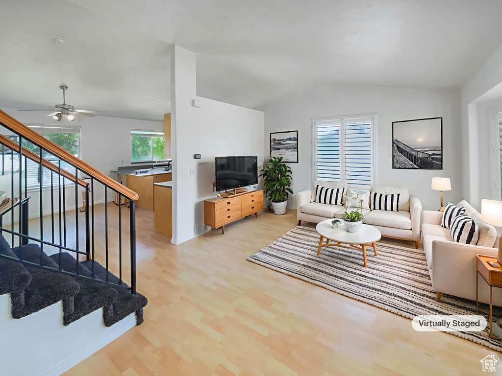 Living area featuring wood finished floors, vaulted ceiling, stairs, a ceiling fan, and baseboards