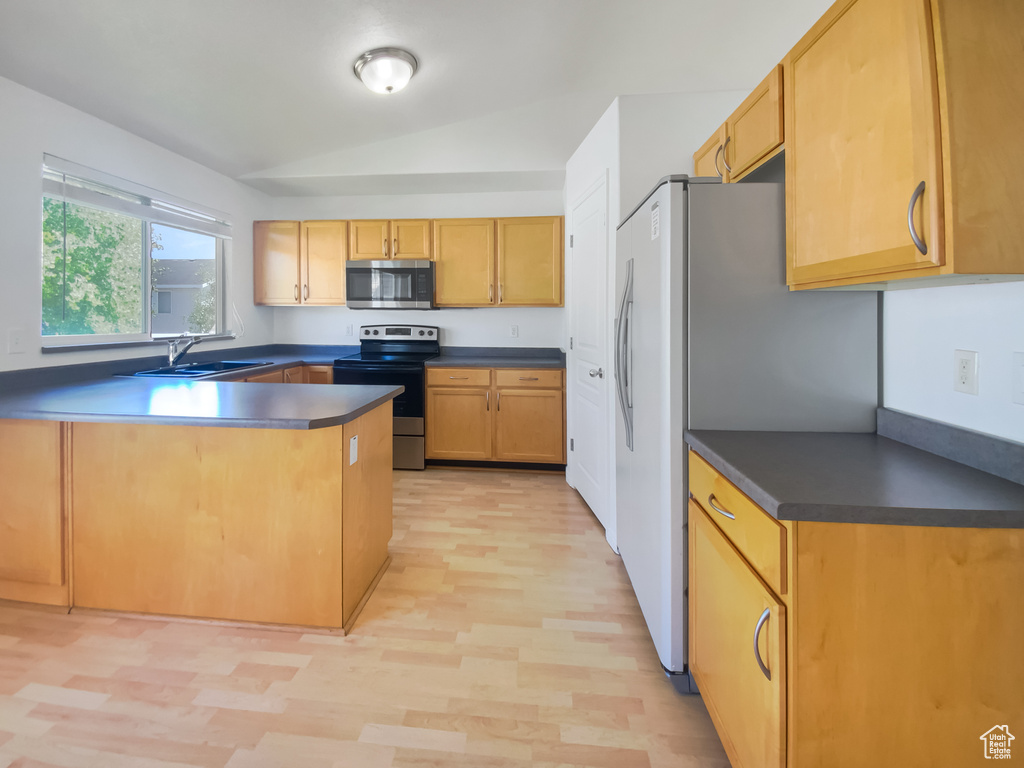 Kitchen featuring stainless steel appliances, a sink, lofted ceiling, a peninsula, and dark countertops