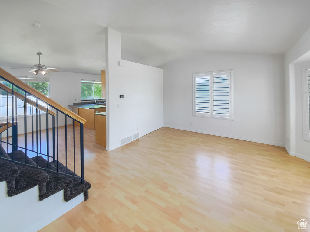 Spare room with light wood-style floors, vaulted ceiling, stairway, a ceiling fan, and baseboards