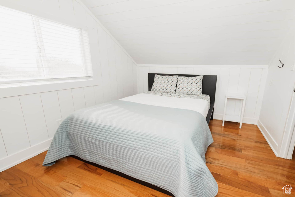 Bedroom with light wood-style floors, vaulted ceiling, and a decorative wall