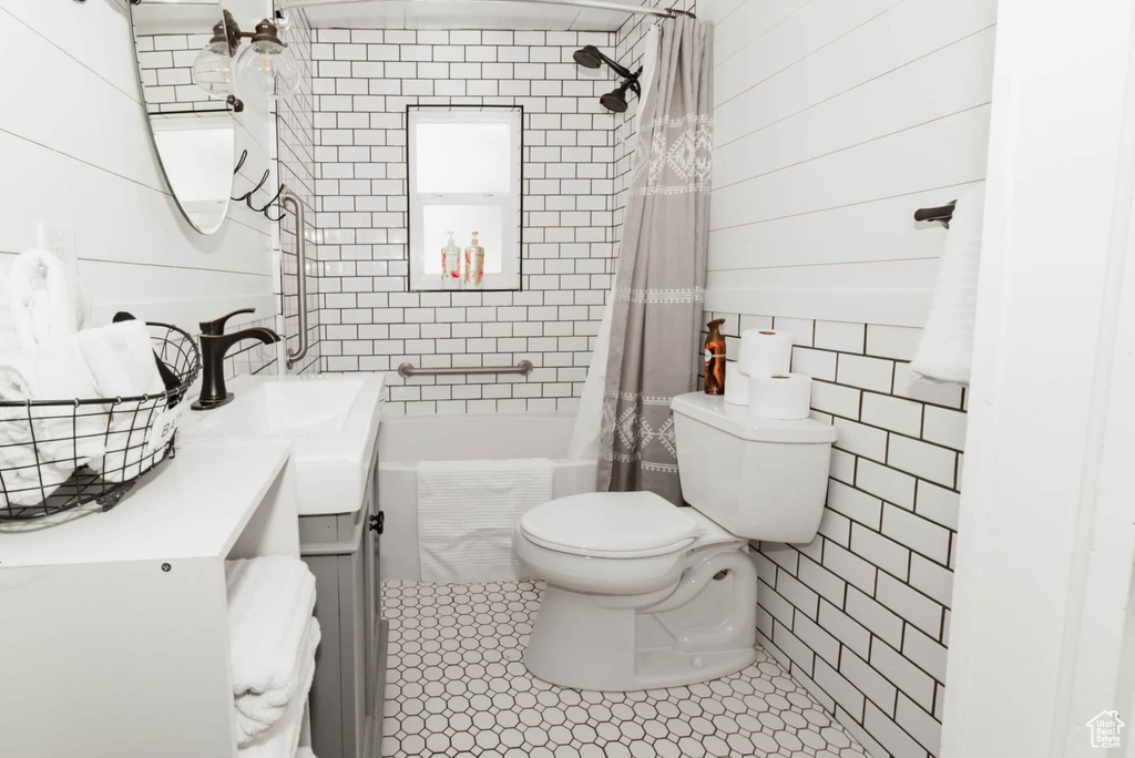 Full bath with tile walls, vanity, toilet, shower / bath combo with shower curtain, and tile patterned floors