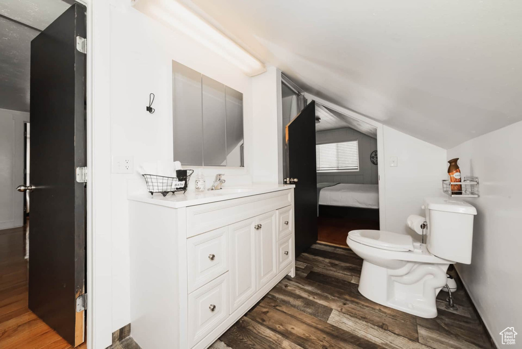 Bathroom with wood finished floors, lofted ceiling, toilet, vanity, and connected bathroom