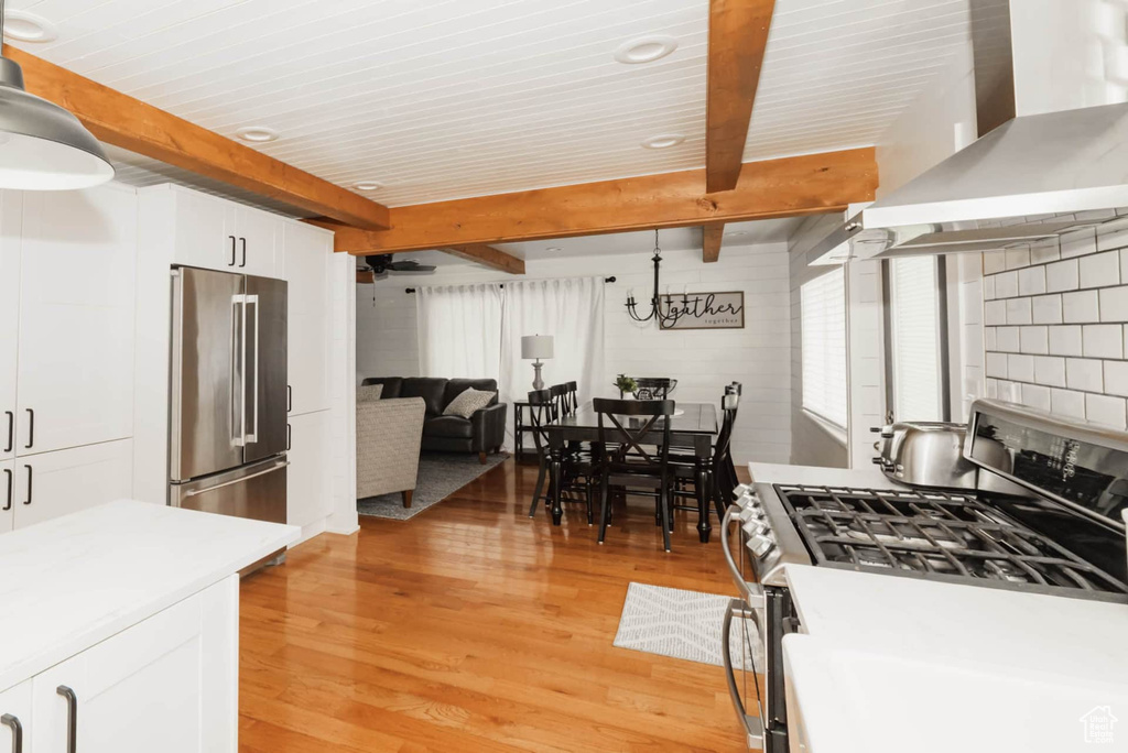 Kitchen with appliances with stainless steel finishes, wall chimney range hood, light wood-style floors, white cabinetry, and light countertops