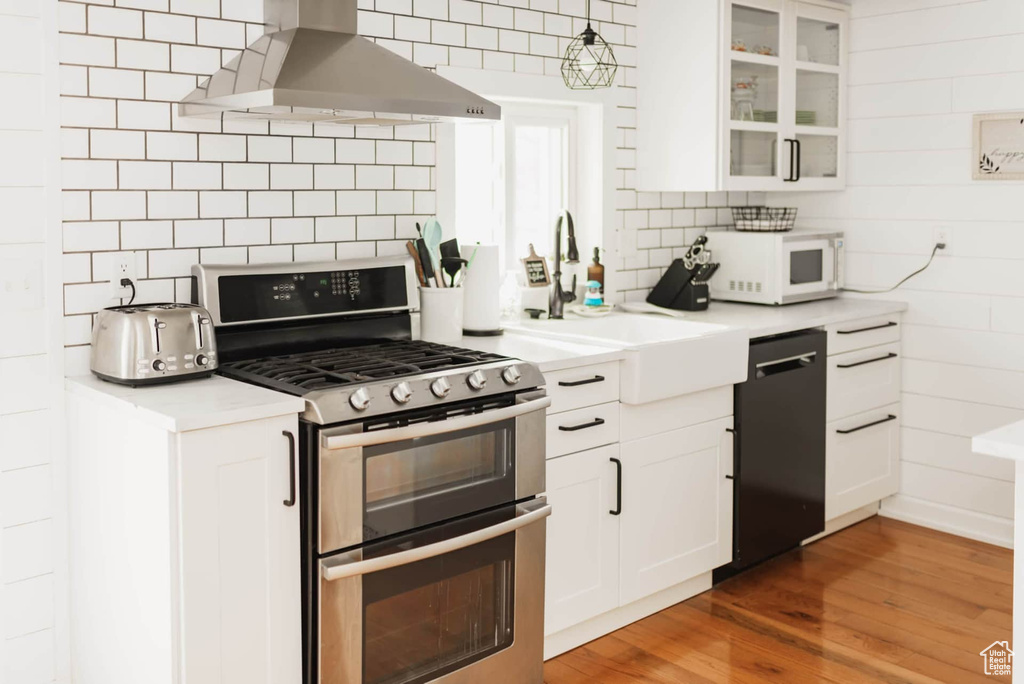 Kitchen featuring range with two ovens, black dishwasher, island exhaust hood, white microwave, and backsplash
