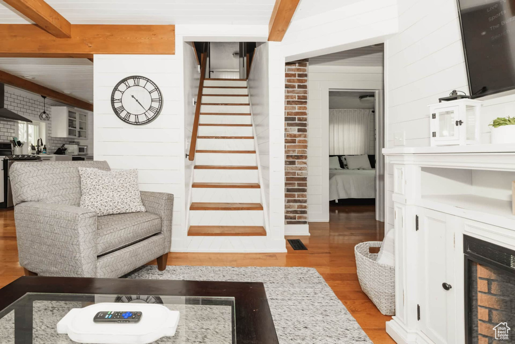 Living room with light wood-type flooring, stairway, beam ceiling, wood walls, and a fireplace