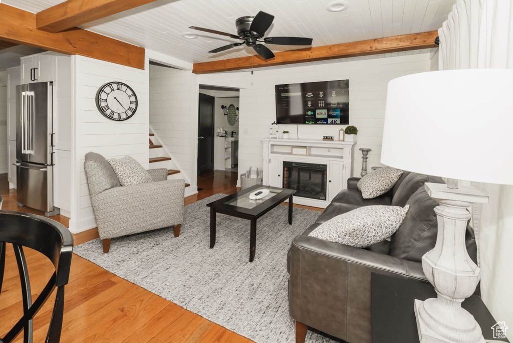 Living room featuring wood finished floors, ceiling fan, a glass covered fireplace, wooden walls, and wooden ceiling with exposed beams