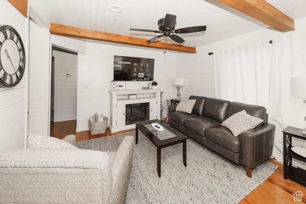 Living area with wood finished floors, a ceiling fan, beamed ceiling, wood walls, and a glass covered fireplace