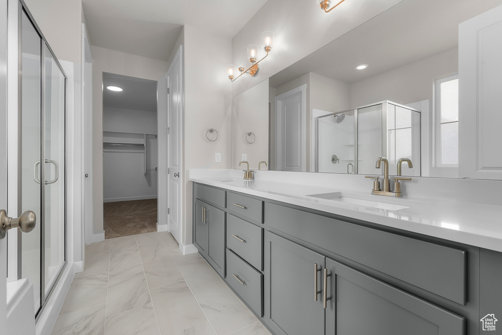 Bathroom featuring marble finish floors, double vanity, a stall shower, a walk in closet, and baseboards