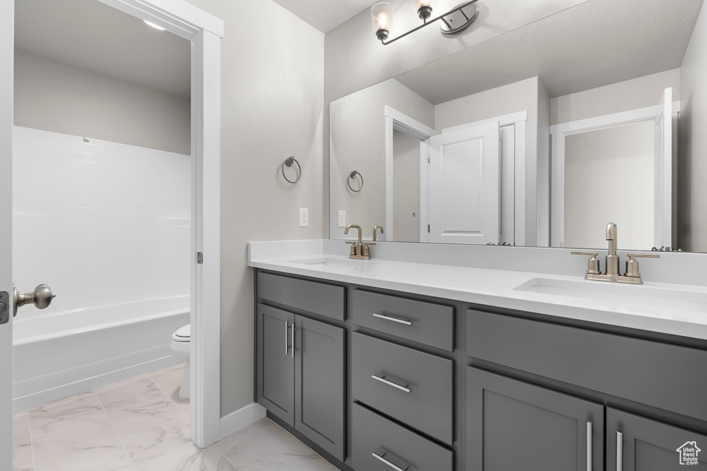 Bathroom with toilet, double vanity, marble look tiles, and baseboards