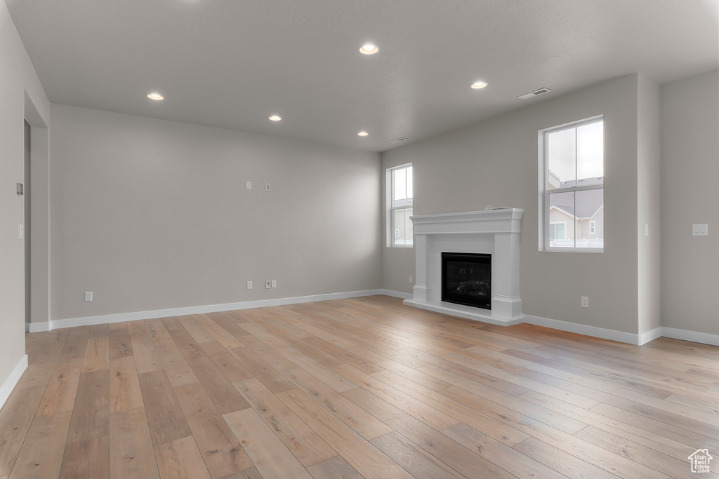 Unfurnished living room with light wood-style flooring, recessed lighting, a glass covered fireplace, and baseboards