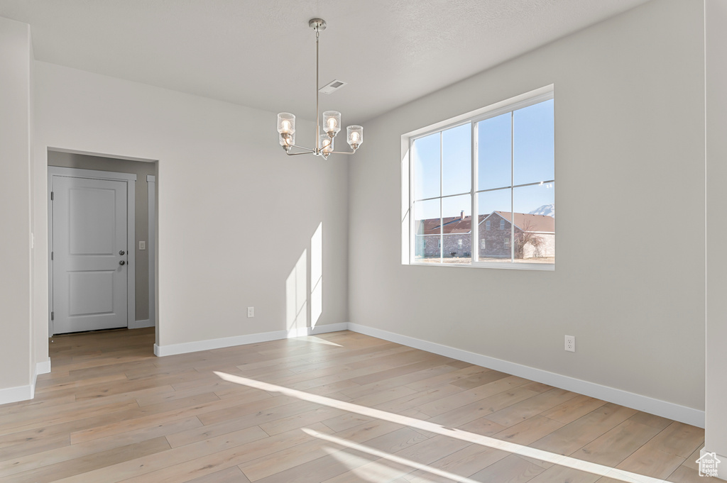 Unfurnished room with a chandelier, light wood-style flooring, and baseboards