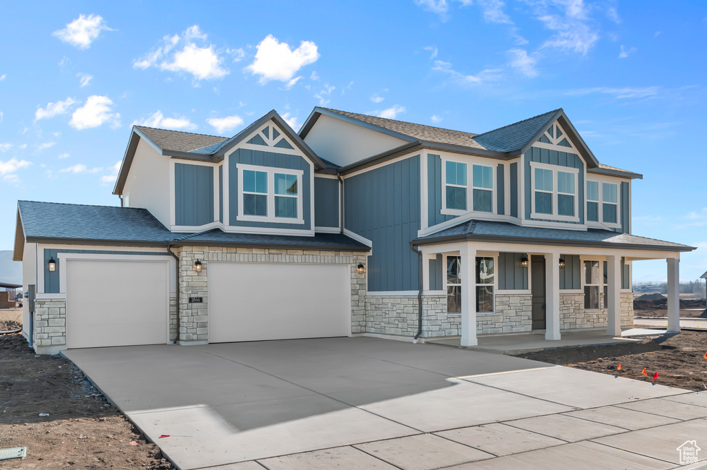 View of front facade featuring stone siding, a porch, concrete driveway, and a shingled roof