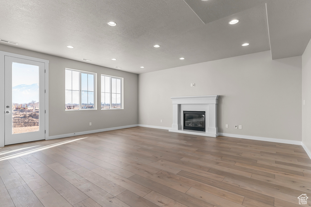 Unfurnished living room with light wood-style floors, a textured ceiling, recessed lighting, a glass covered fireplace, and baseboards