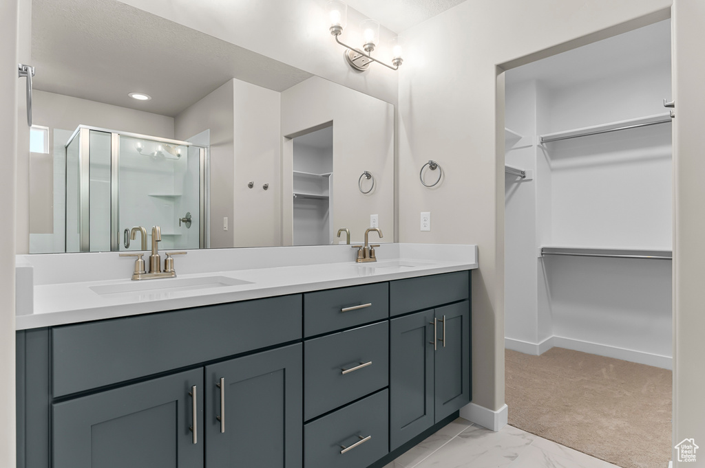 Full bathroom with a walk in closet, double vanity, a shower stall, baseboards, and marble finish flooring