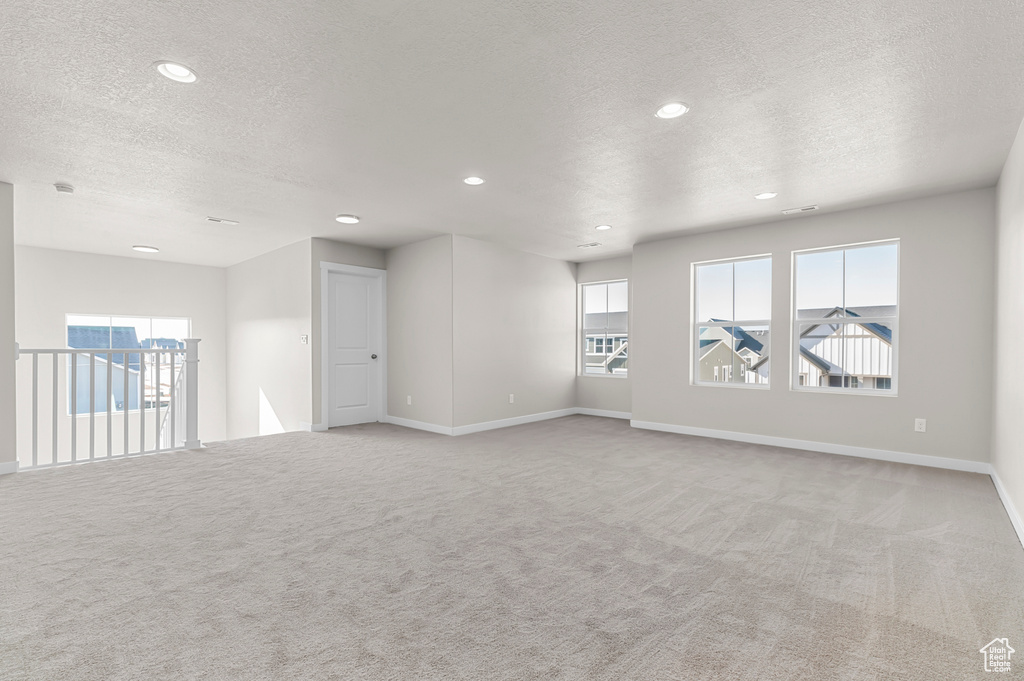 Empty room with light colored carpet, a textured ceiling, baseboards, and recessed lighting