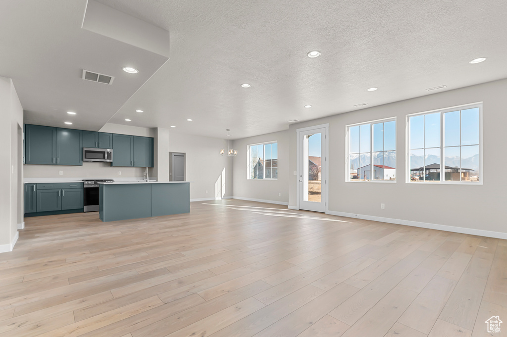 Unfurnished living room featuring a chandelier, baseboards, recessed lighting, light wood-style flooring, and a textured ceiling