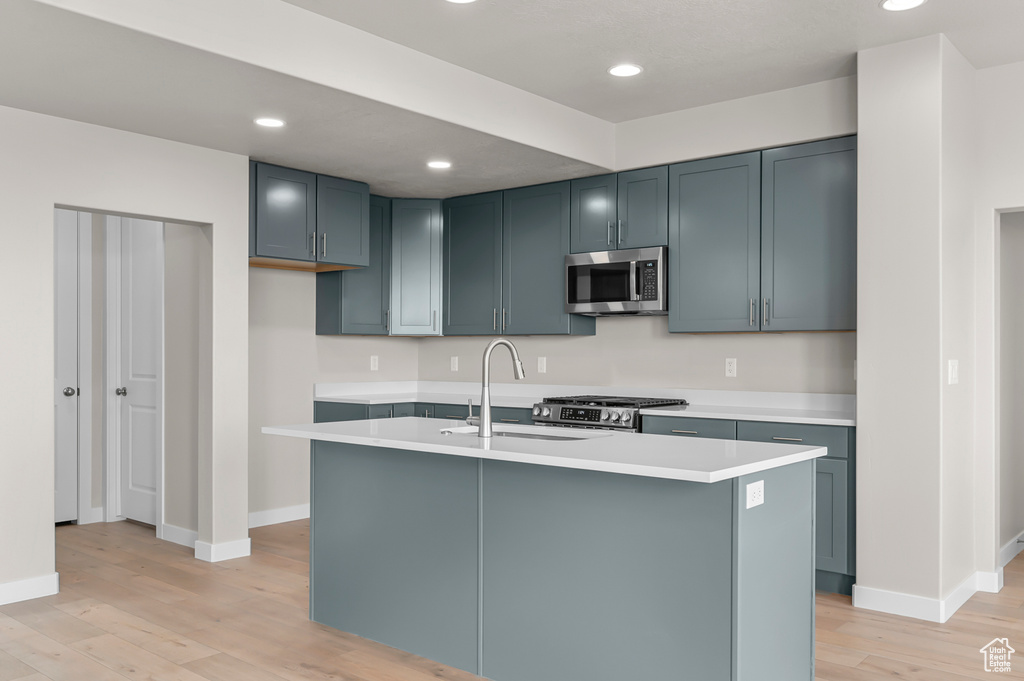 Kitchen with appliances with stainless steel finishes, a sink, light wood-style floors, light countertops, and baseboards
