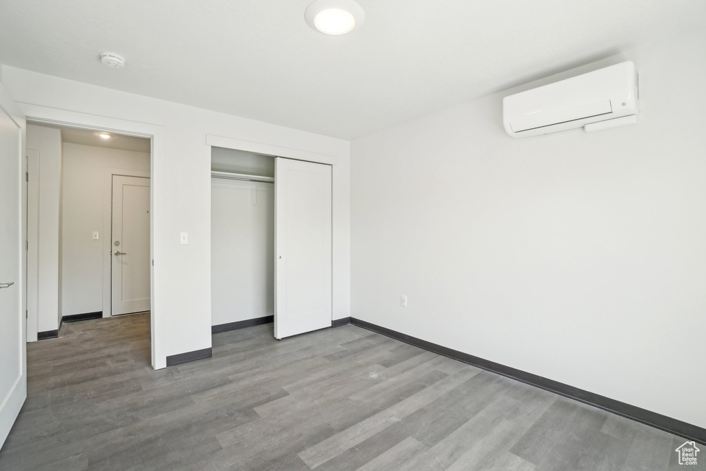 Unfurnished bedroom with a wall unit AC, wood finished floors, baseboards, and a closet