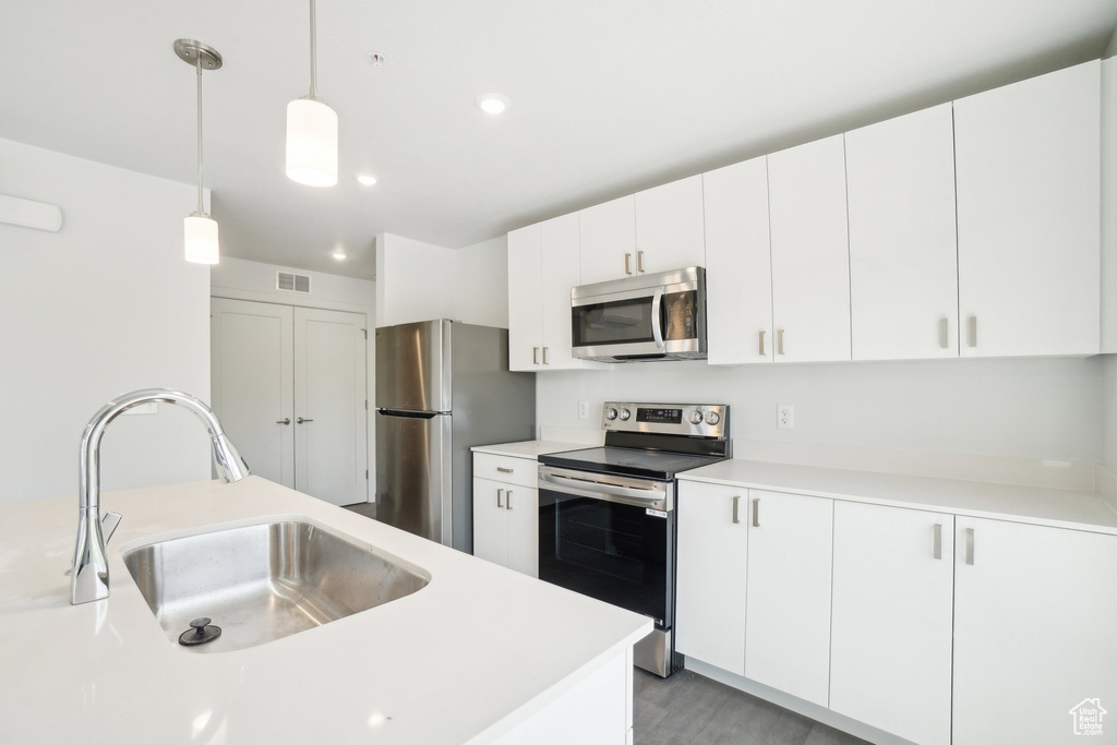 Kitchen featuring appliances with stainless steel finishes, a sink, light countertops, hanging light fixtures, and white cabinetry