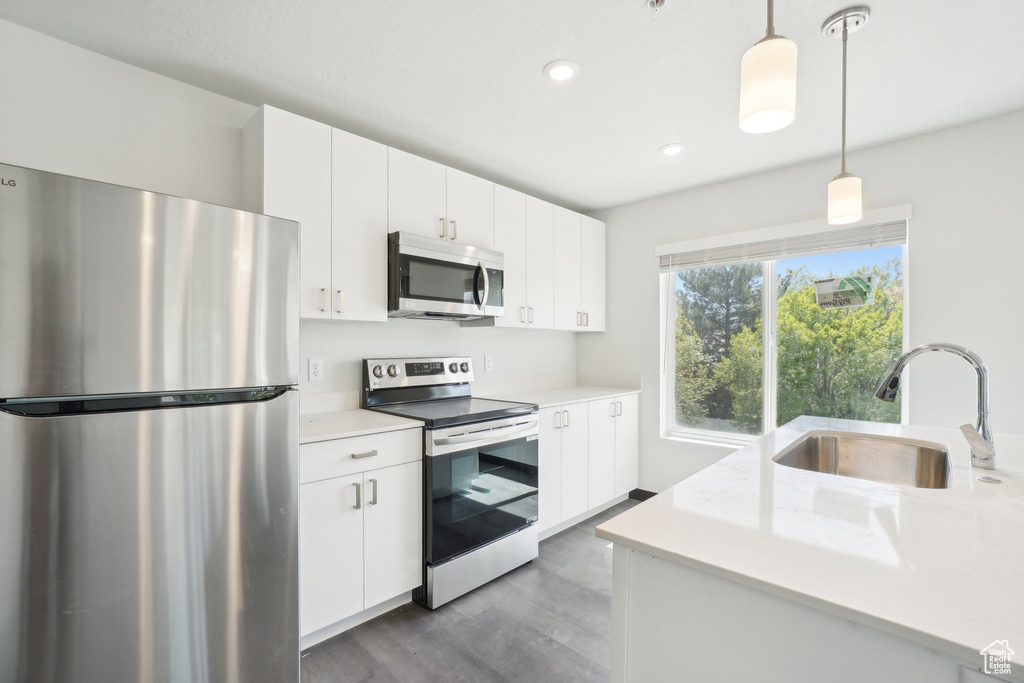 Kitchen with stainless steel appliances, a sink, light countertops, hanging light fixtures, and wood finished floors