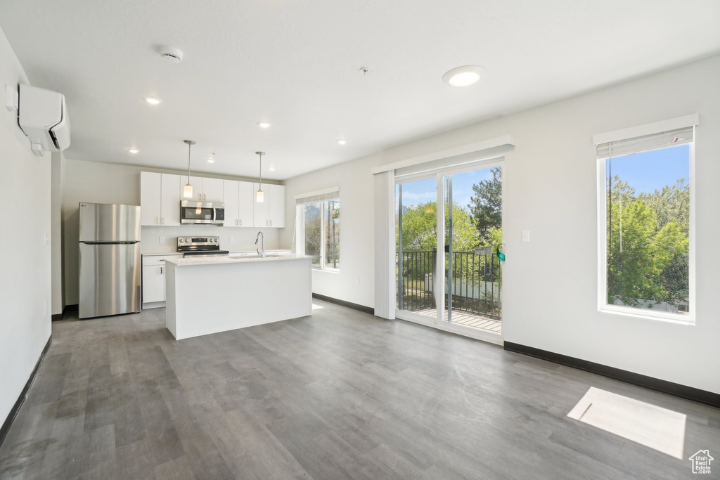Kitchen with appliances with stainless steel finishes, a sink, an AC wall unit, white cabinets, and dark wood-style flooring
