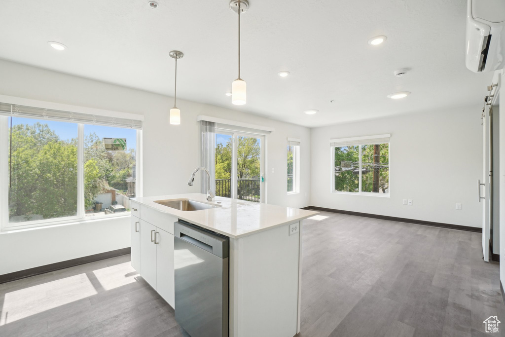 Kitchen featuring dishwasher, a sink, light wood-type flooring, a wall mounted air conditioner, and hanging light fixtures