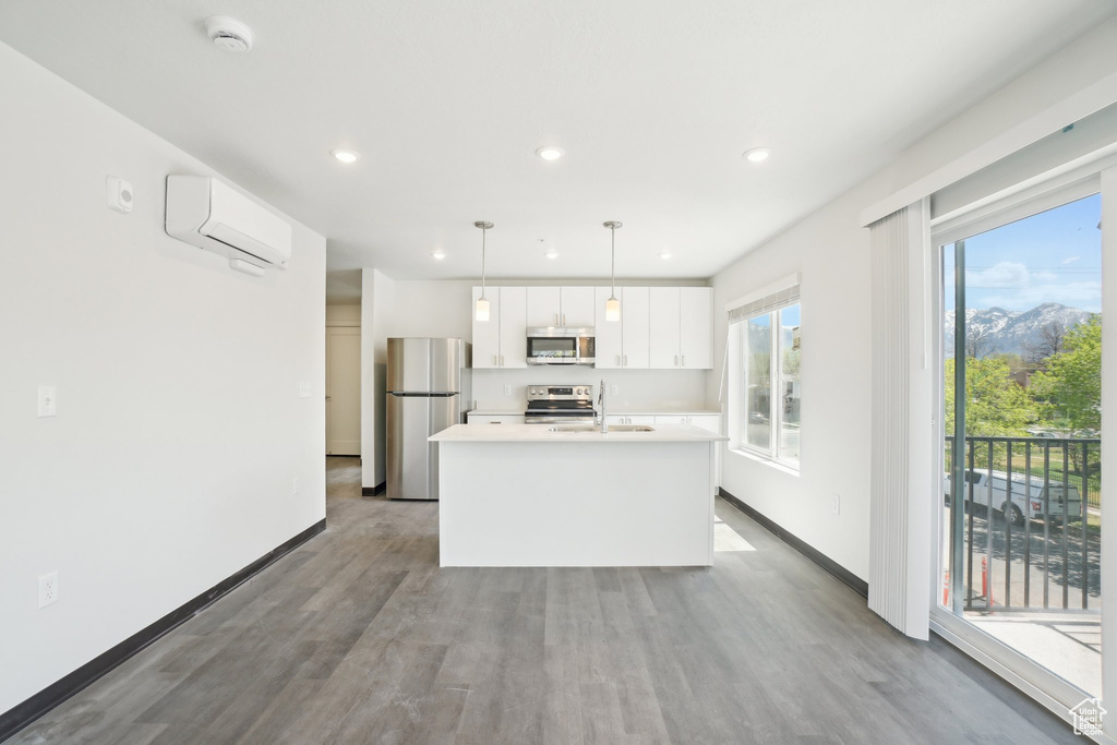 Kitchen with stainless steel appliances, white cabinets, a center island with sink, a sink, and light countertops