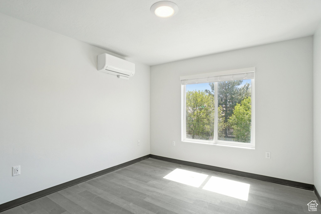 Unfurnished room with a wall unit AC, wood finished floors, and baseboards