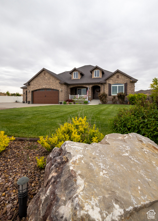 View of front of house with an attached garage, a front lawn, a porch, and brick siding