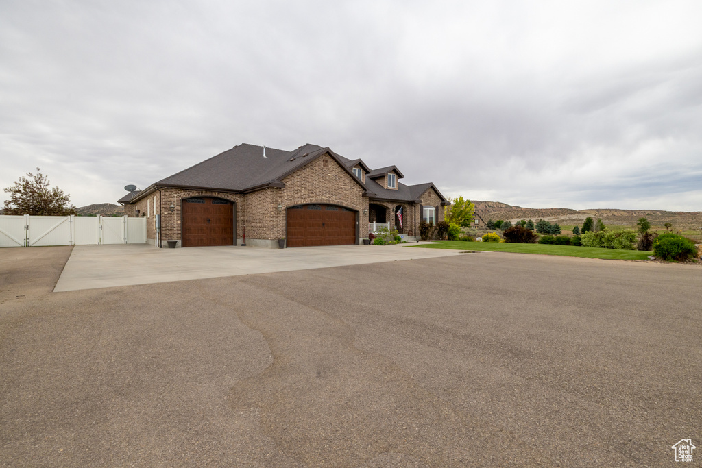 French country home with a gate, a garage, brick siding, and asphalt driveway