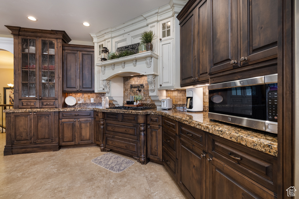 Kitchen featuring stainless steel microwave, arched walkways, dark brown cabinetry, black gas stovetop, and decorative backsplash