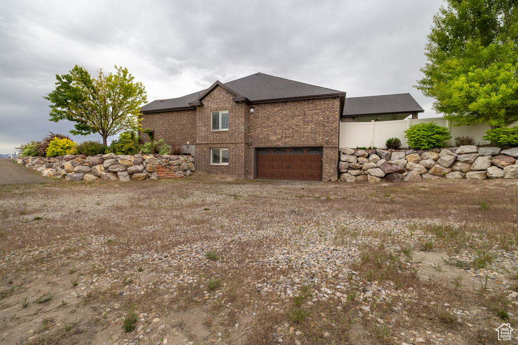 View of side of home with brick siding, dirt driveway, and a garage