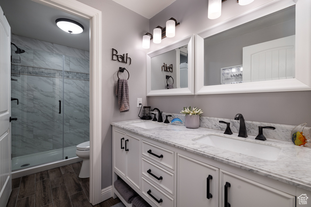 Bathroom with double vanity, a shower stall, toilet, and wood finished floors