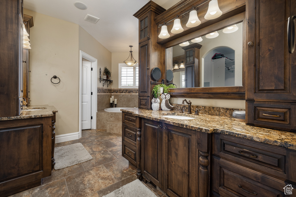 Full bathroom featuring two vanities, stone tile floors, a garden tub, and baseboards