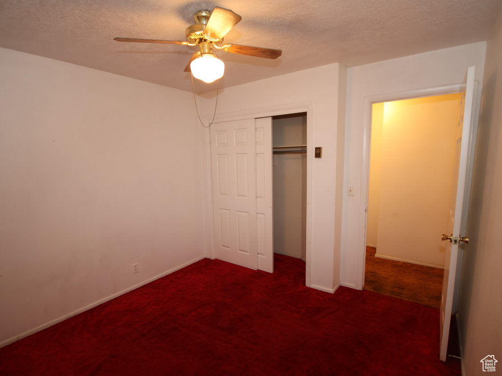 Unfurnished bedroom featuring dark carpet, a closet, baseboards, a ceiling fan, and a textured ceiling