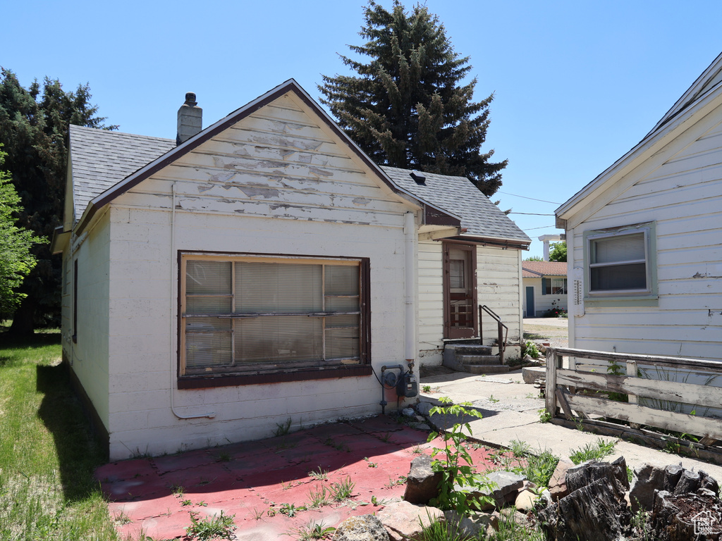 Back of house with entry steps, a shingled roof, a chimney, and a patio area