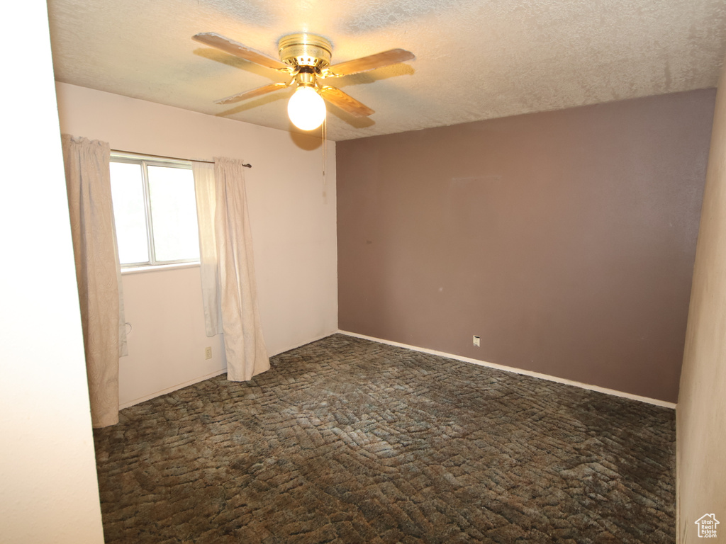 Unfurnished room featuring dark carpet, ceiling fan, and a textured ceiling