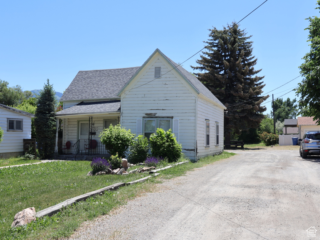 View of front facade with roof with shingles, a porch, driveway, and a front yard