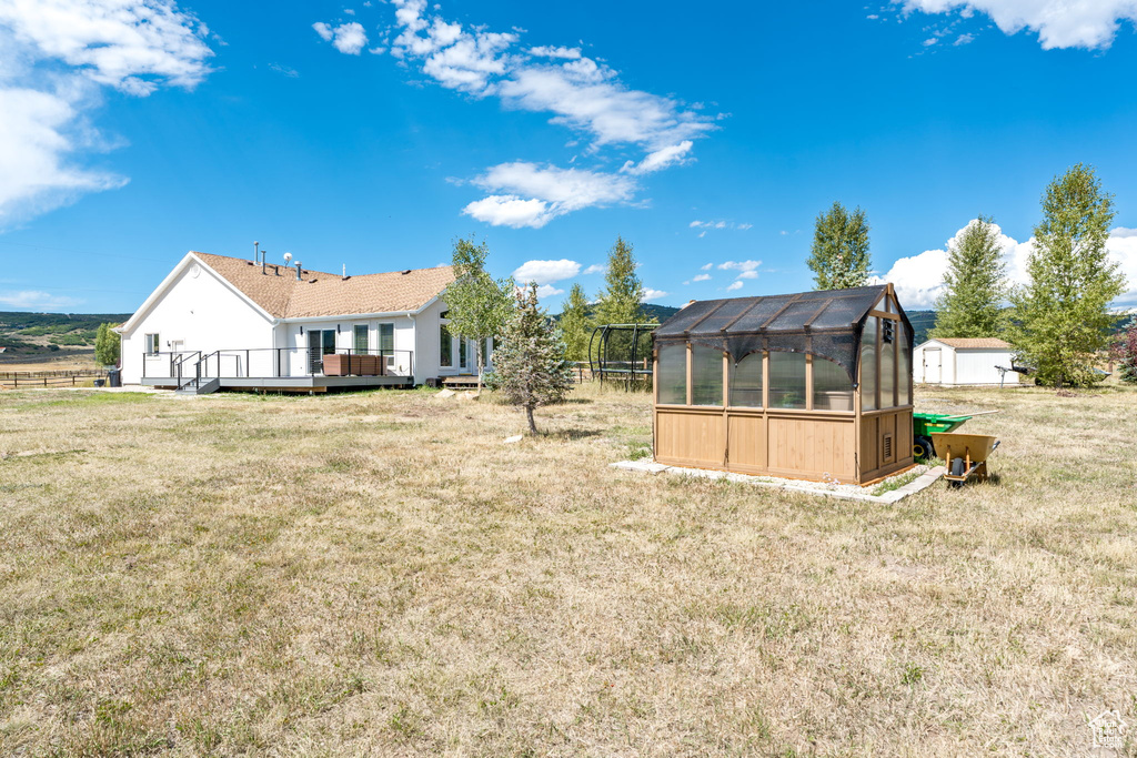 Rear view of property featuring a greenhouse, an outdoor structure, a deck, and a lawn