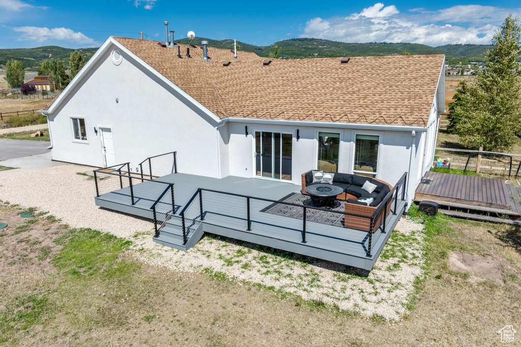 Back of property featuring a deck with mountain view, stucco siding, an outdoor living space with a fire pit, and roof with shingles