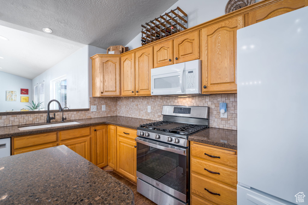 Kitchen featuring white appliances, a sink, vaulted ceiling, decorative backsplash, and a textured ceiling