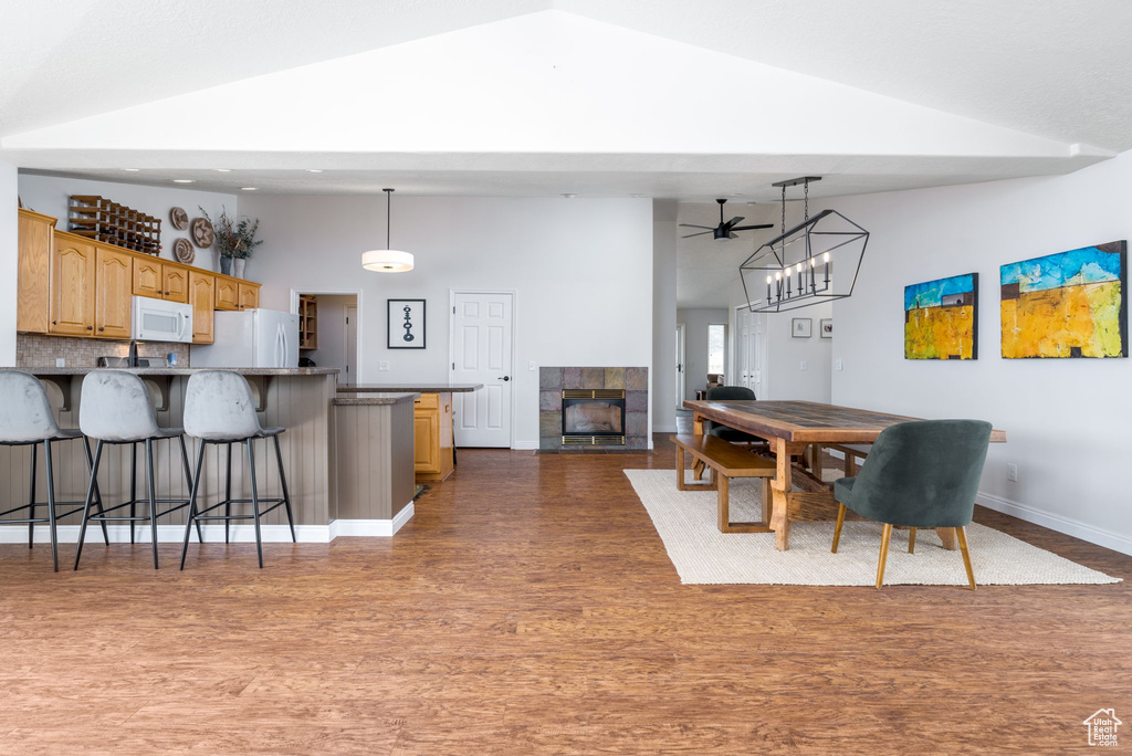 Dining room featuring high vaulted ceiling, wood finished floors, a ceiling fan, baseboards, and a fireplace