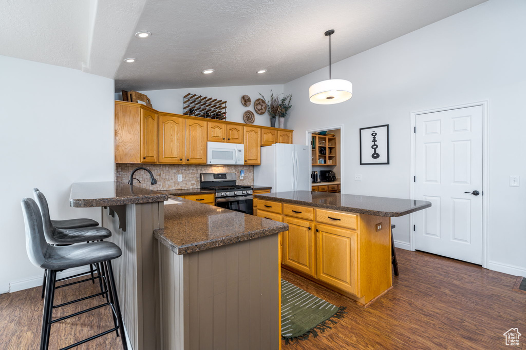 Kitchen with white appliances, vaulted ceiling, a kitchen breakfast bar, tasteful backsplash, and dark wood-type flooring