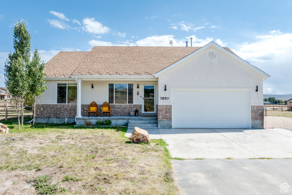 Single story home with brick siding, an attached garage, covered porch, and concrete driveway