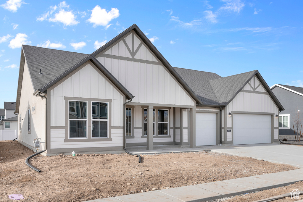 View of front of property with covered porch, roof with shingles, an attached garage, driveway, and board and batten siding