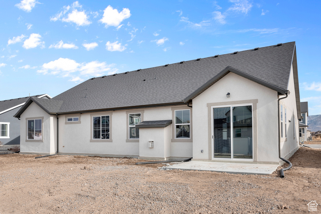 Back of property with stucco siding, a shingled roof, and a patio area