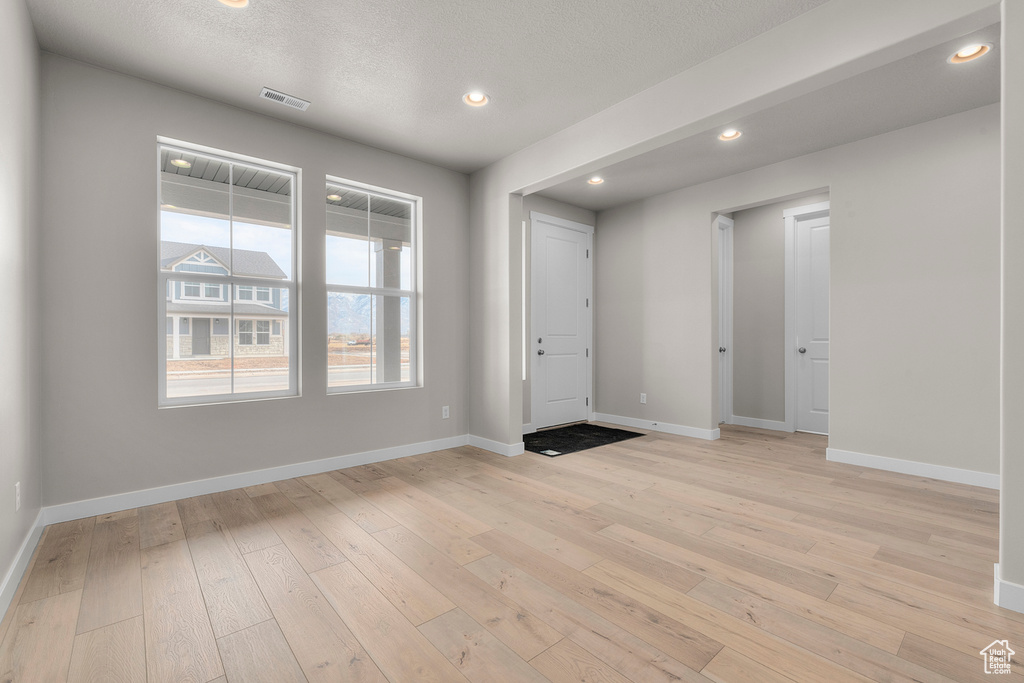 Foyer entrance with light wood finished floors, baseboards, recessed lighting, and a textured ceiling