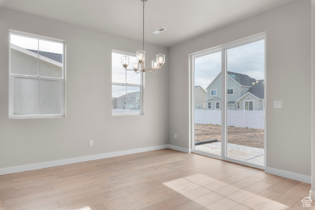 Unfurnished room with a chandelier, plenty of natural light, light wood finished floors, and baseboards