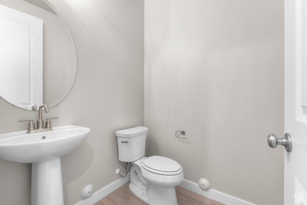 Half bathroom featuring toilet, baseboards, wood finished floors, and a sink