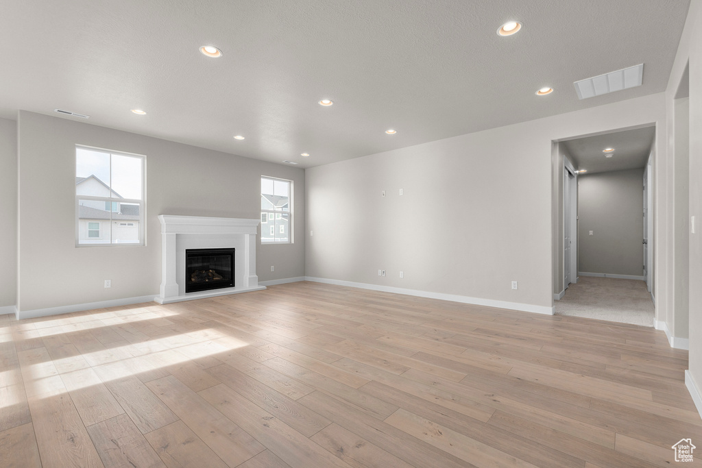 Unfurnished living room with light wood finished floors, recessed lighting, a glass covered fireplace, and baseboards